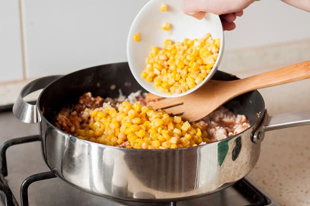 консервированная кукуруза добавляется в сковороду с кусочками куриного филе и лопаткой