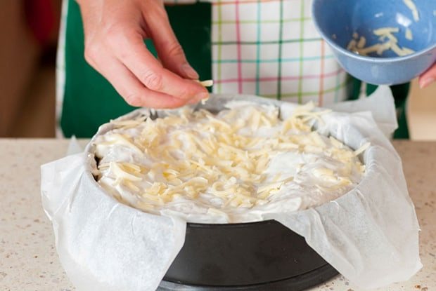 заготовка из лаваша, смазанная сметаной, в форме для запекания посыпается тертым сыром